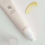 Närbild på Beauty of Joseon Revive Eye Serum-tub och en klick av det gula serumet på en ljus yta.