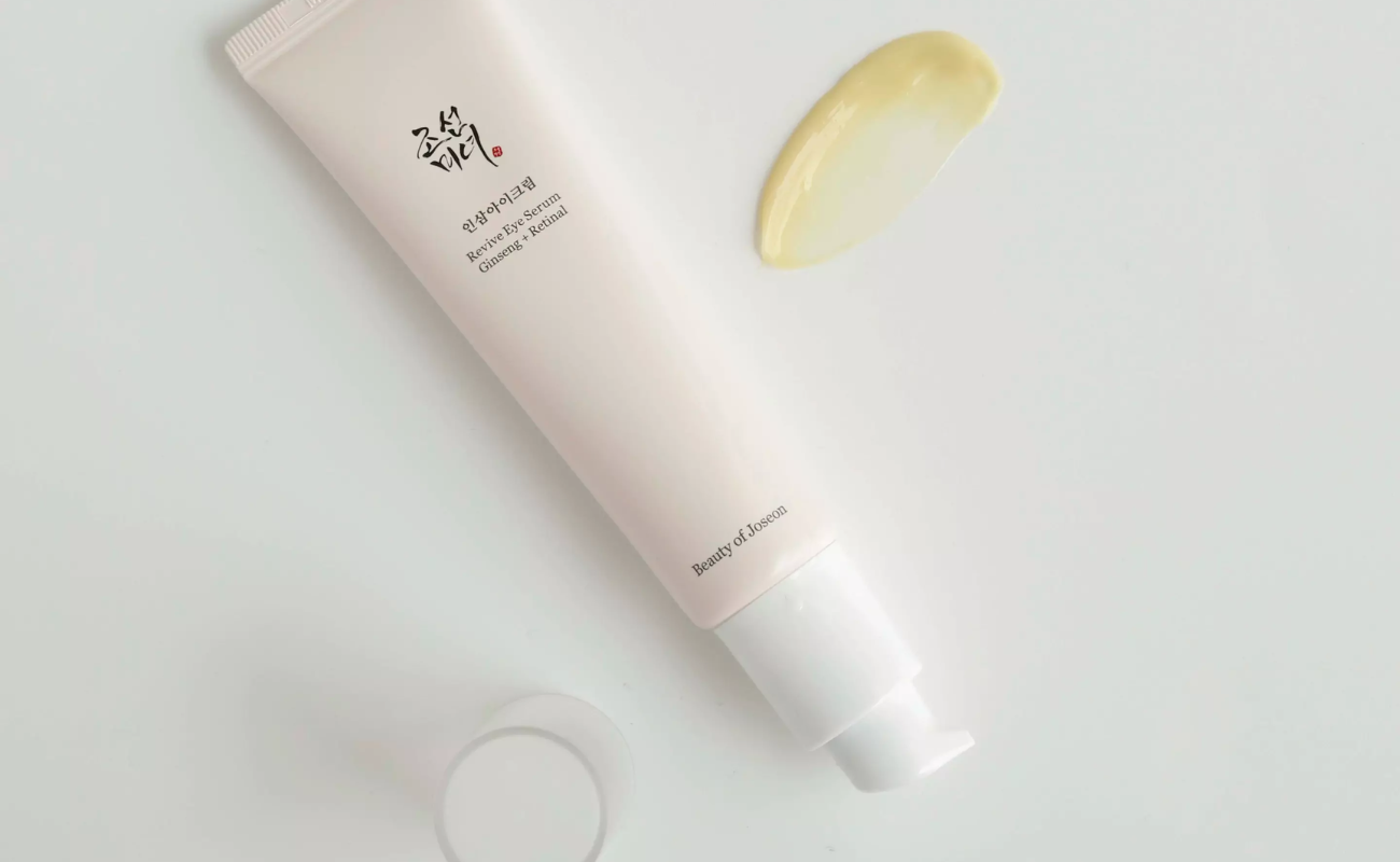 Närbild på Beauty of Joseon Revive Eye Serum-tub och en klick av det gula serumet på en ljus yta.