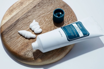 Närbild på Klairs Rich Moist Soothing Cream-tub och klickar av vit ansiktskräm på ett träfat.