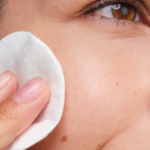 Närbild på applicering av ansiktsvatten med bomullsrondell på kinden för exfoliering.